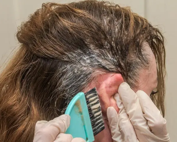 Manos enguantadas aplican tinte en el cabello. Si te manchas la piel, aprende como quitar el tinte de la piel fácilmente.