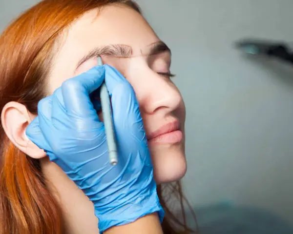 Manos enguantadas dibujan cejas a una mujer pelirroja. ¡No tengo cejas que puedo hacer!