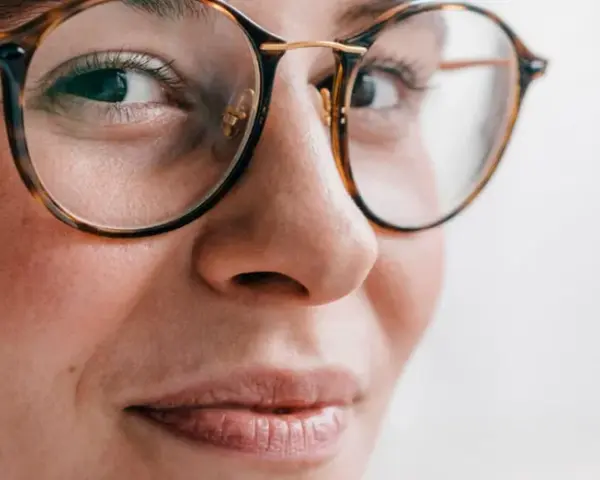 Primer plano de una mujer con gafas de montura de carey, sus ojos hundidos miran hacia un lado con una leve sonrisa.