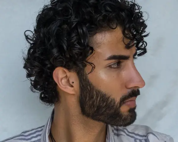 Hombre con cabello rizado y barba. Su peinado luce como si se preguntara cuanto dura una permanente rizada hombre.