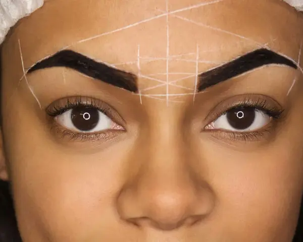 Ojos y cejas marcadas con líneas blancas para diseño. Se observa una posible alergia a la henna en las cejas.