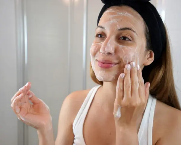 Mujer con diadema negra aplicándose espuma en el rostro, parte de su rutina de limpieza facial.