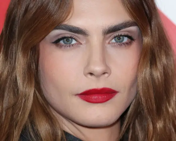 Primer plano de una mujer con cejas pobladas y labios rojos. ¿Recortar cejas sí o no? La decisión es tuya.