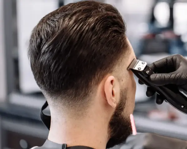 Barbero creando un tuper fade impecable en la nuca de un cliente.