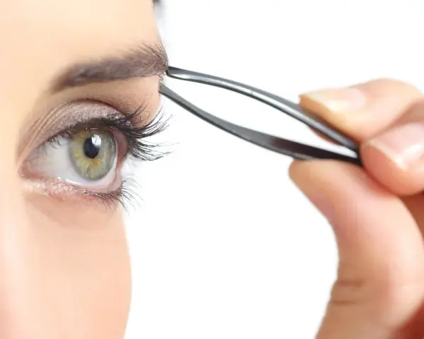 Ojo verde con pestaña larga, depilándose la ceja con pinzas. Decide cada cuanto depilarse las cejas para un look perfecto.