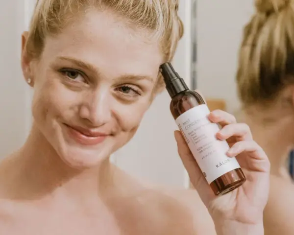 Mujer sonriente aplica bruma facial para como fijar el maquillaje. El producto es de la marca KÁLOS.