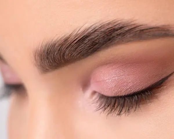 Ojo cerrado con sombra rosa, delineado cat eye y cejas separadas bien definidas.