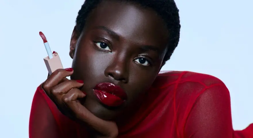 Mujer con labios rojos brillantes y un aplicador de brillo labial. Sus cejas rojas resaltan su mirada intensa.