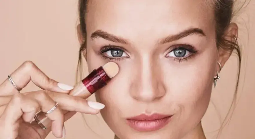 Mujer aplicando corrector para maquillar bolsas ojos. Suave aplicador y piel radiante.