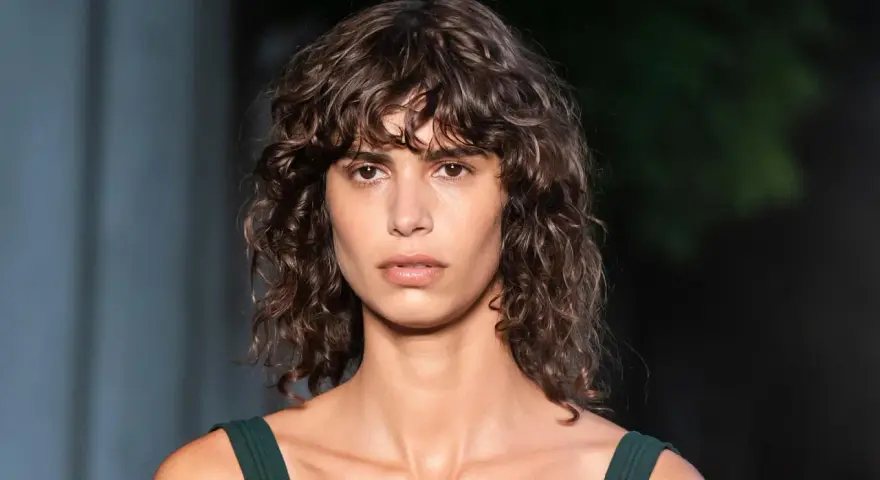 Mujer con pelo rizado y flequillo despeinado, un ejemplo de los tipos de flequillo para pelo rizado que realzan la textura natural.
