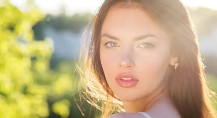 Rostro de mujer con cabello castaño y ojos verdes, iluminado por el sol. Su expresión transmite un glow up, un renacer radiante.