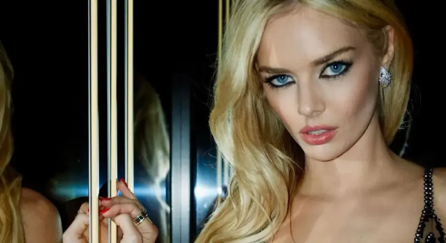 Maquillaje ojos verdes boda: rubia con ojos azules intensos, labios rosados y vestido negro brillante.