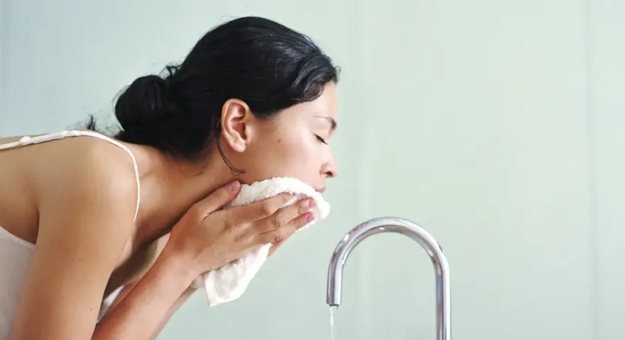 Mujer se limpia el rostro con una toalla suave, como si el agua micelar se enjuaga.