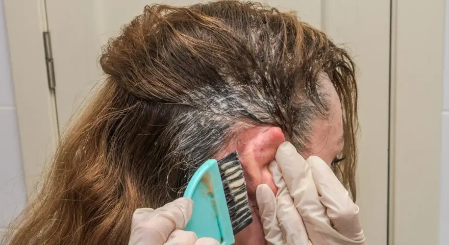 Manos enguantadas aplican tinte en el cabello. Si te manchas la piel, aprende como quitar el tinte de la piel fácilmente.