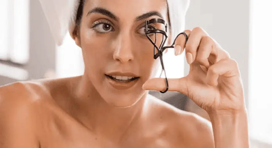 Mujer con toalla en la cabeza usa un rizador de pestañas. A veces, el rizador de pestañas es malo para tus ojos.