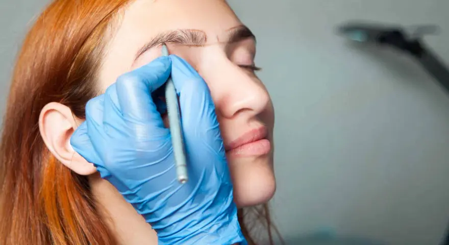 Manos enguantadas dibujan cejas a una mujer pelirroja. ¡No tengo cejas que puedo hacer!