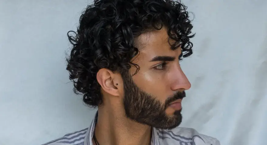 Hombre con cabello rizado y barba. Su peinado luce como si se preguntara cuanto dura una permanente rizada hombre.
