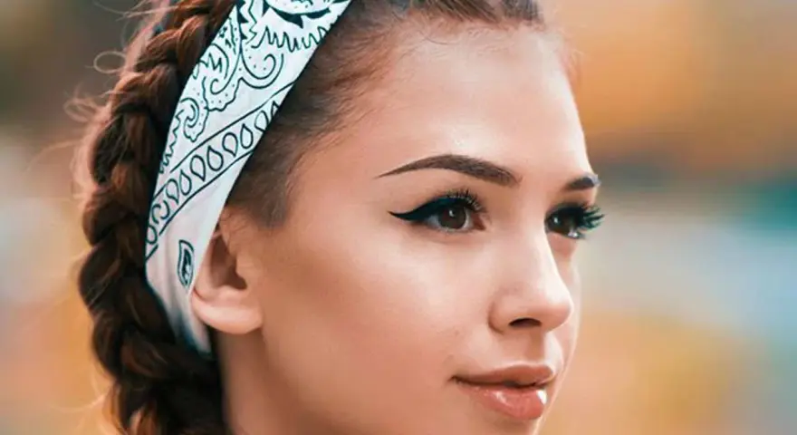 Chica con trenzas y pañuelo, mostrando cómo pintar la raya del ojo con delineado cat eye perfecto.