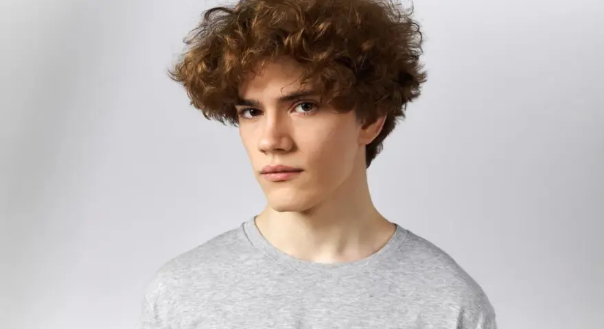 Joven con un moderno corte de pelo rizado hombre, luciendo un estilo desenfadado y juvenil.