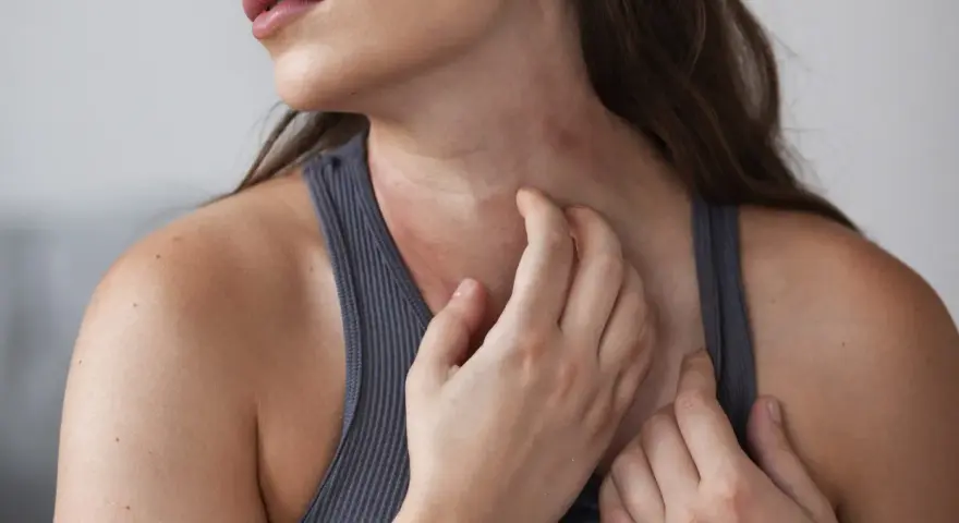 Mujer rascándose el cuello, mostrando varios tipos de manchas en el cuello, posiblemente por irritación o alergia.