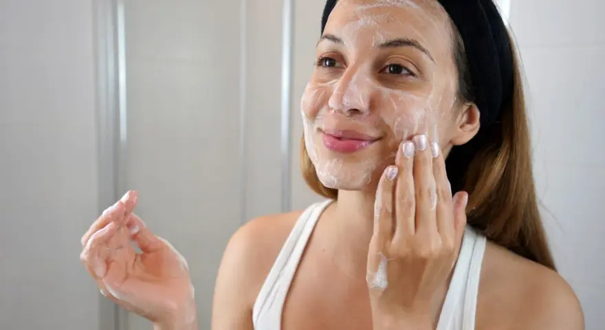 Mujer con diadema negra aplicándose espuma en el rostro, parte de su rutina de limpieza facial.
