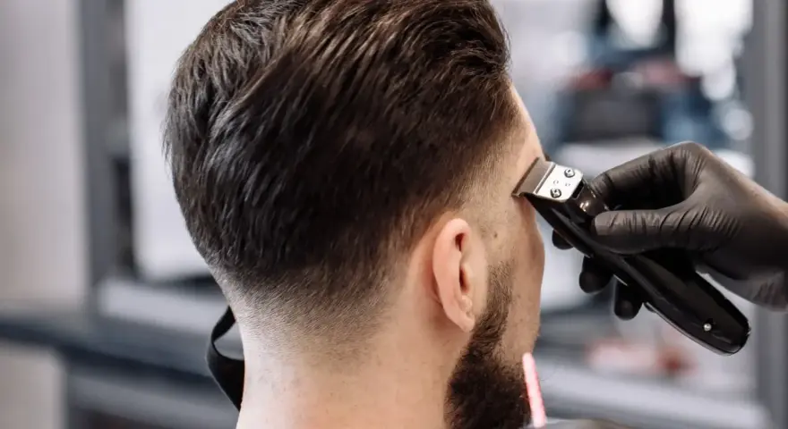 Barbero creando un tuper fade impecable en la nuca de un cliente.