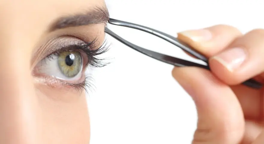 Ojo verde con pestaña larga, depilándose la ceja con pinzas. Decide cada cuanto depilarse las cejas para un look perfecto.