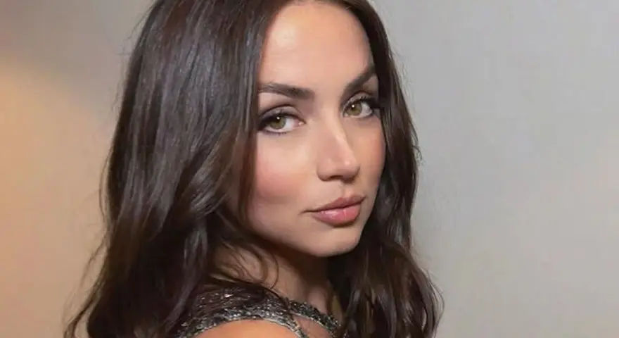 Mujer con cortes de pelo ondulado castaño, mirada intensa y vestido brillante.