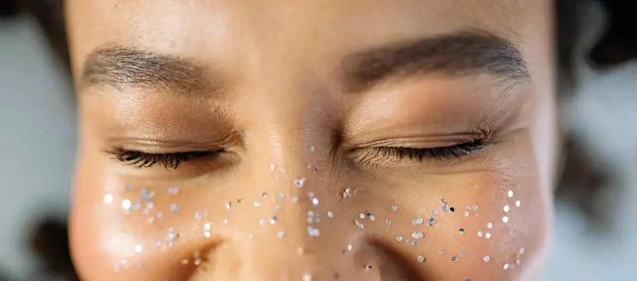 Ojos cerrados con purpurina en las mejillas. Las cejas bien definidas sugieren que la persona sabe cada cuanto depilarse las cejas para mantener este look.