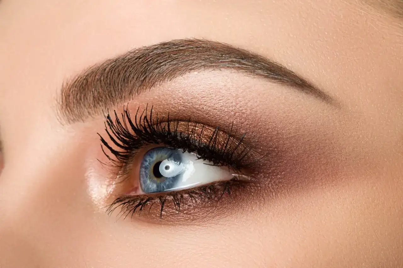 Ojo azul con maquillaje marrón y pestañas largas. Las cejas perfectamente definidas sugieren un proceso de teñir cejas profesional.