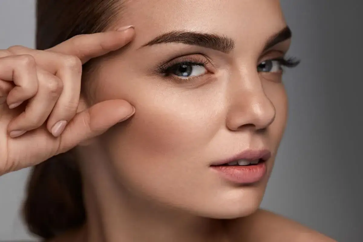 Primer plano de una mujer con cejas rectas y definidas, su mano toca suavemente su sien.