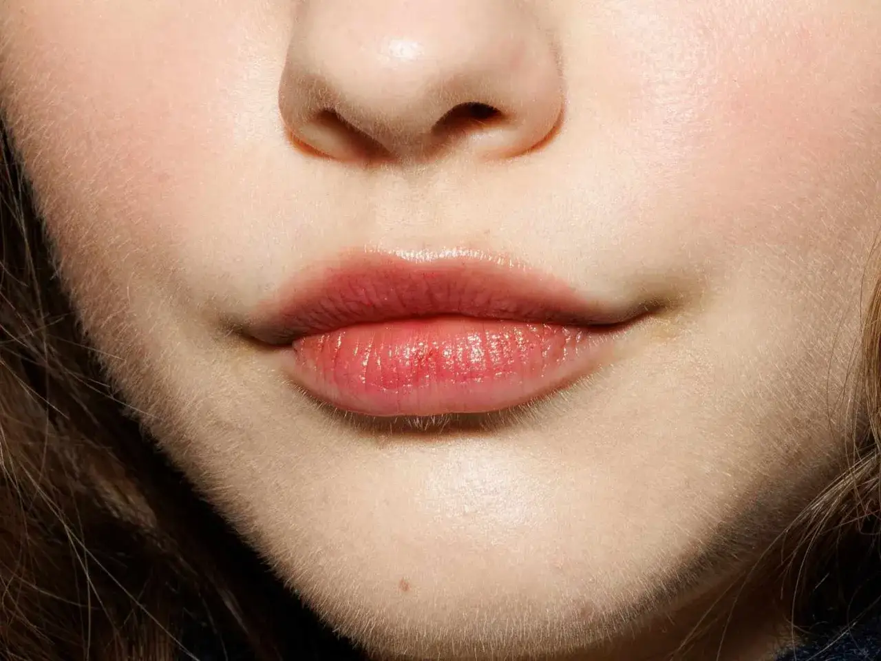 Labios rosados y brillantes, con un ligero brillo. Se aprecian pequeños granos en los labios, parte de la textura natural de la piel.