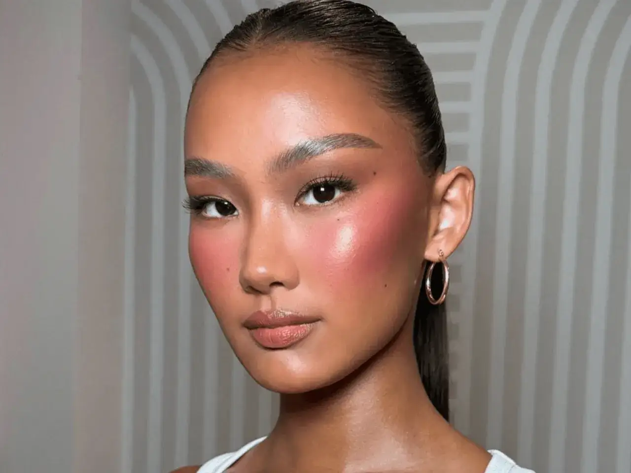 Rostro de mujer con un radiante maquillaje cálido, mejillas sonrosadas y labios naturales.