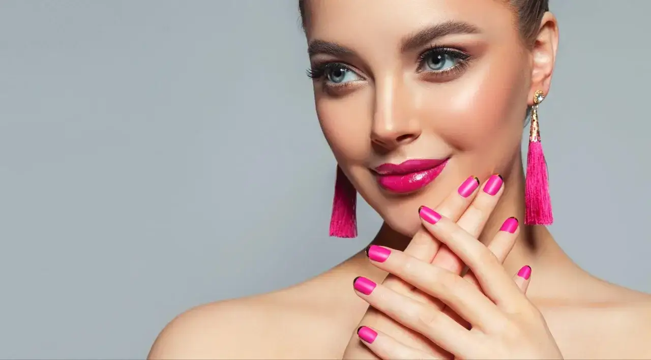 Maquillaje vibrante con labios fucsia y uñas a juego, ideal para un vestido fucsia. Pendientes largos y llamativos complementan el look.