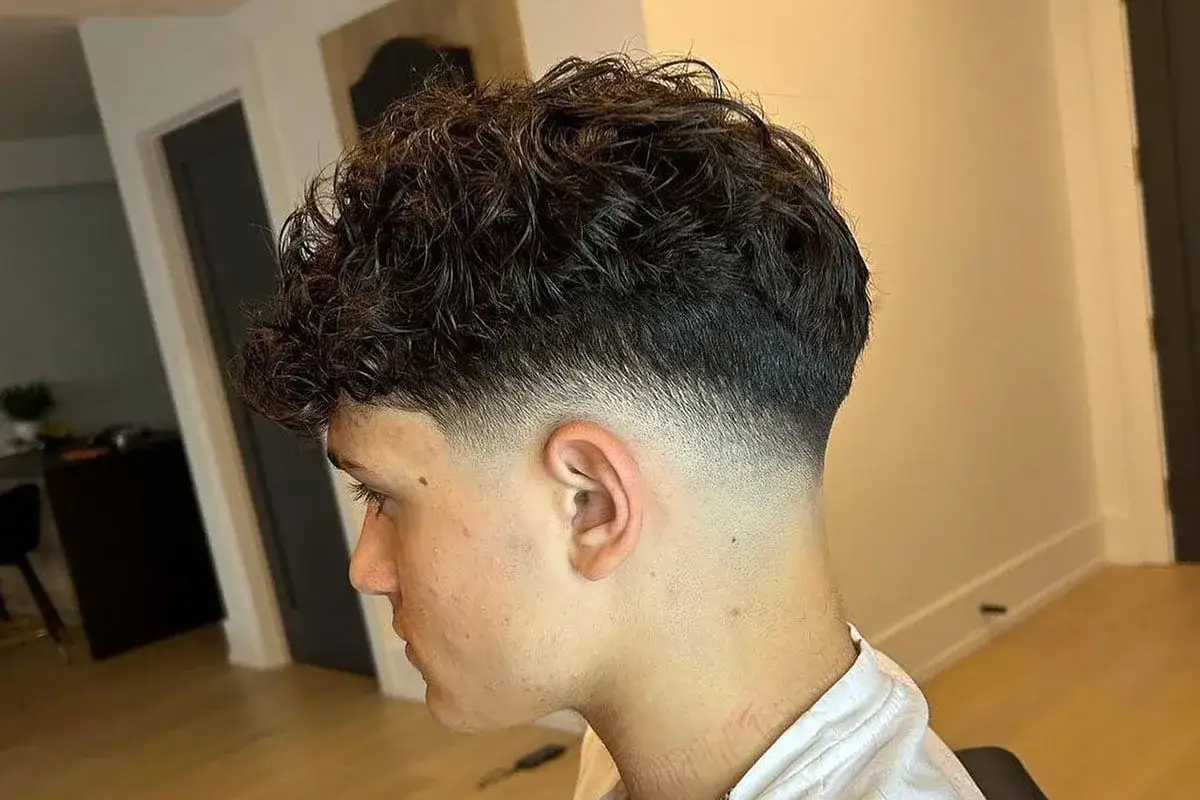 Joven con cabello rizado oscuro y un corte moderno con desvanecido bajo impecable.