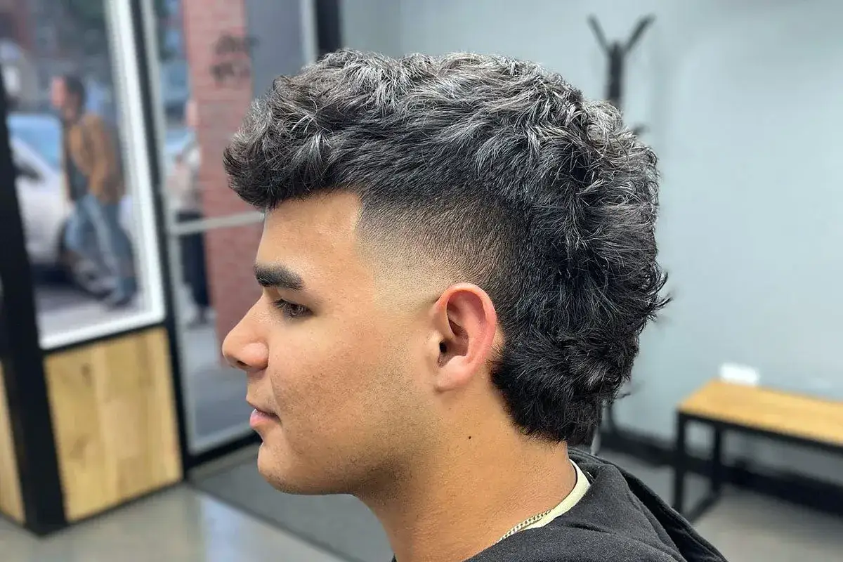 Joven con un corte de pelo moderno, uno de los tipos de mullet, con degradado en los laterales y pelo rizado en la parte superior y trasera.