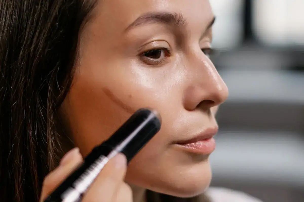 Mujer aplicando producto para un contouring tutorial. Se ve la línea de contorno en su mejilla.