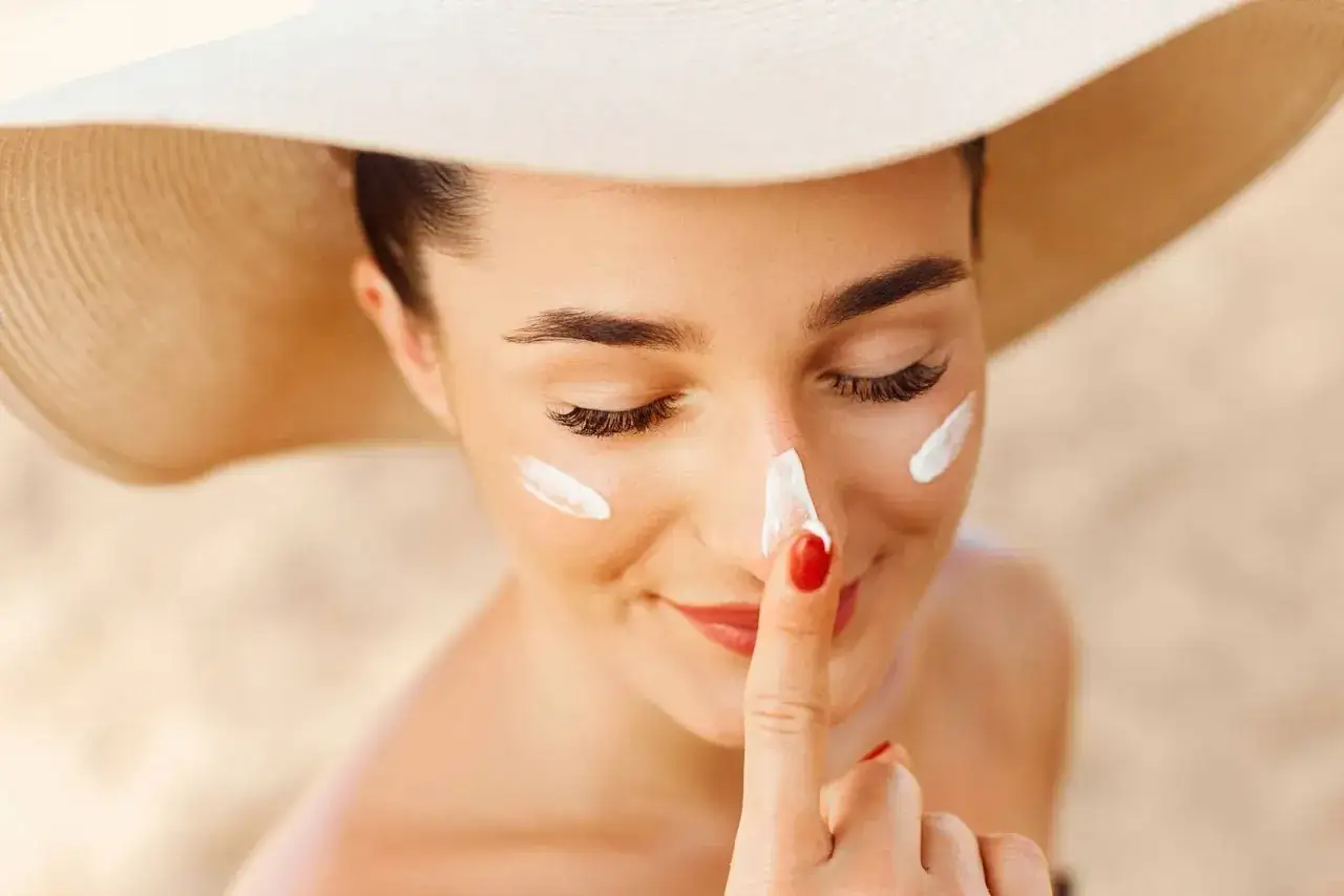Mujer con sombrero aplicando crema solar en la nariz. Se puede usar despigmentante en verano para proteger la piel.