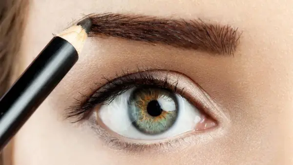 Detalle de ojo y ceja siendo maquillada con lápiz para disimular calvas.