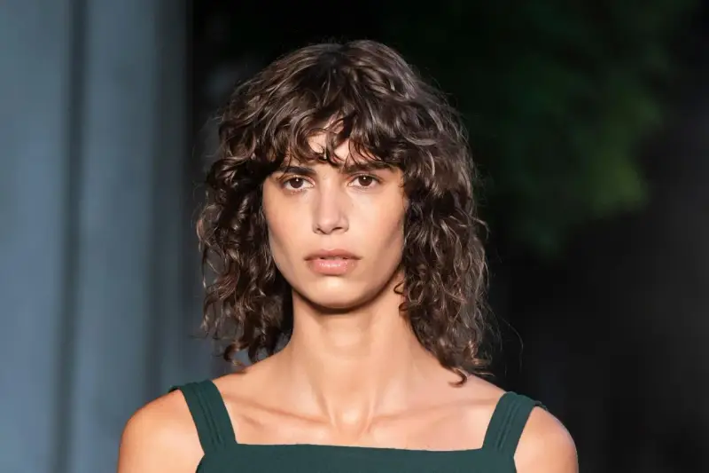 Mujer con pelo rizado y flequillo despeinado, un ejemplo de los tipos de flequillo para pelo rizado que realzan la textura natural.