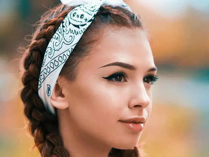 Chica con trenzas y pañuelo, mostrando cómo pintar la raya del ojo con delineado cat eye perfecto.