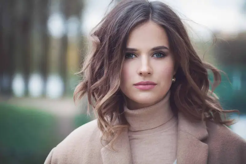Mujer con peinados media melena elegantes, ondas suaves y un abrigo beige.