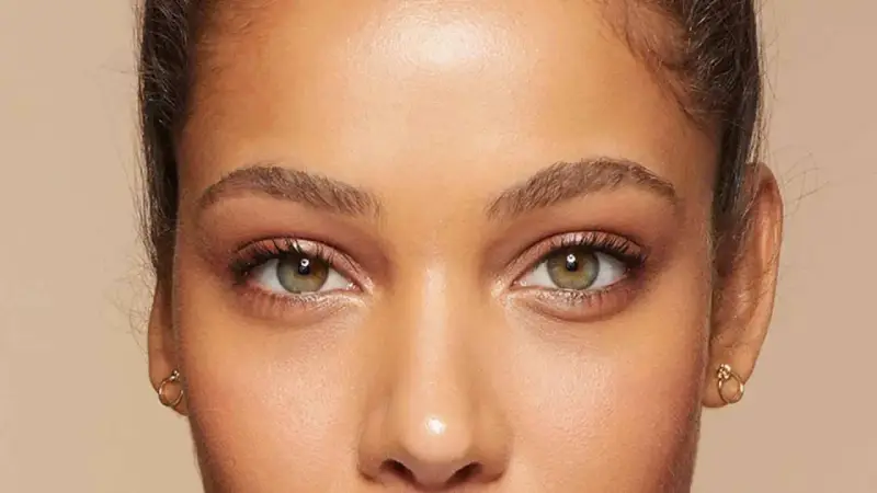 Primer plano de unos ojos verdes y marrones, mostrando cómo cambiar la forma de las cejas con maquillaje.